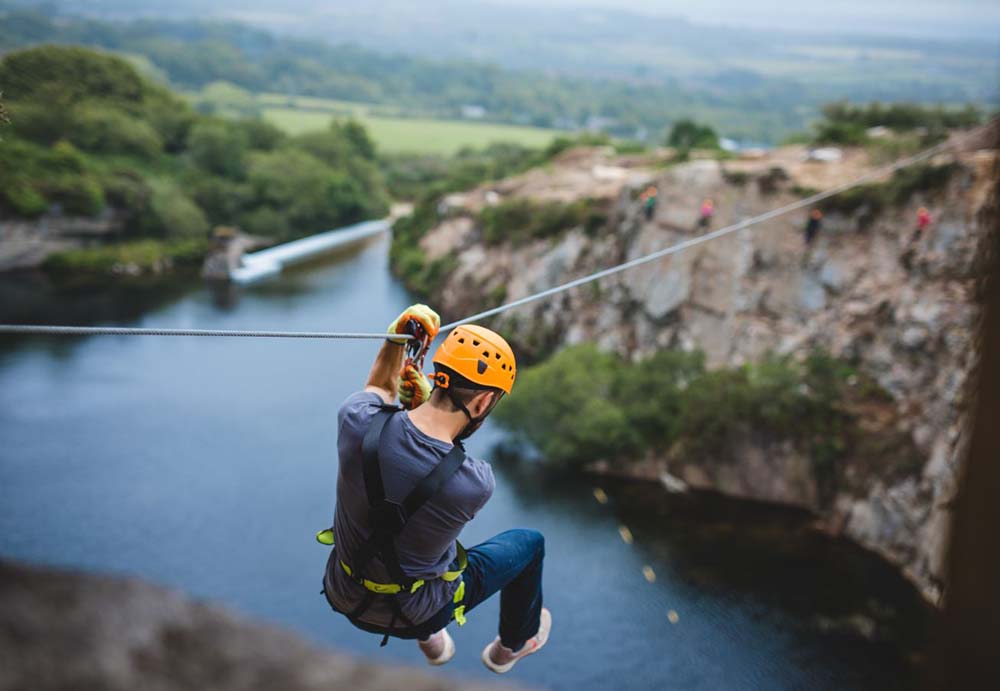 Man leaping off cliffs on a zip wire in Cornwall at Via Ferrata Cornwall