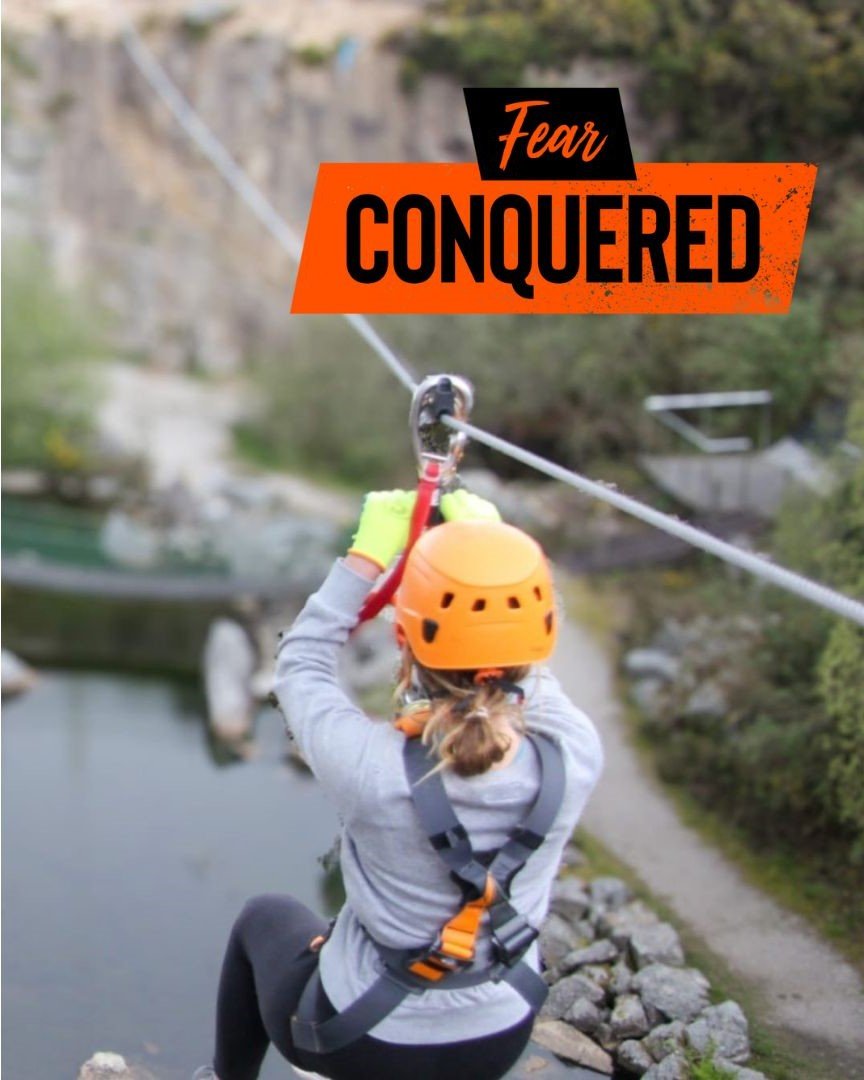 photo of women/girl on a zip wire over a quarry with water below. Over the photo is the text 'Fear Conquered'